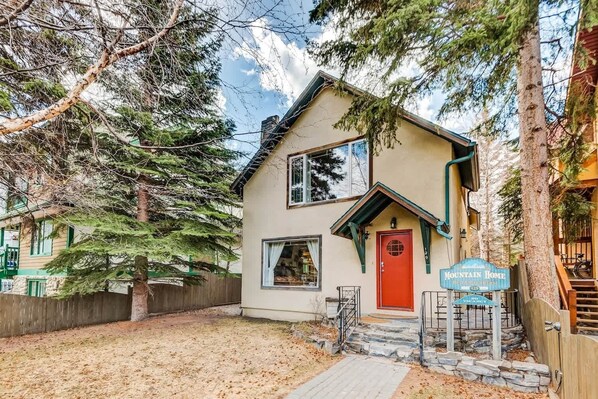 A two-story house with a red door, a sign indicating 'MOUNTAIN HOME' and 'VACANCY', and a stone staircase leading to the entrance. - Banff Mountain Home- The Real Rockies Experience (Banff)