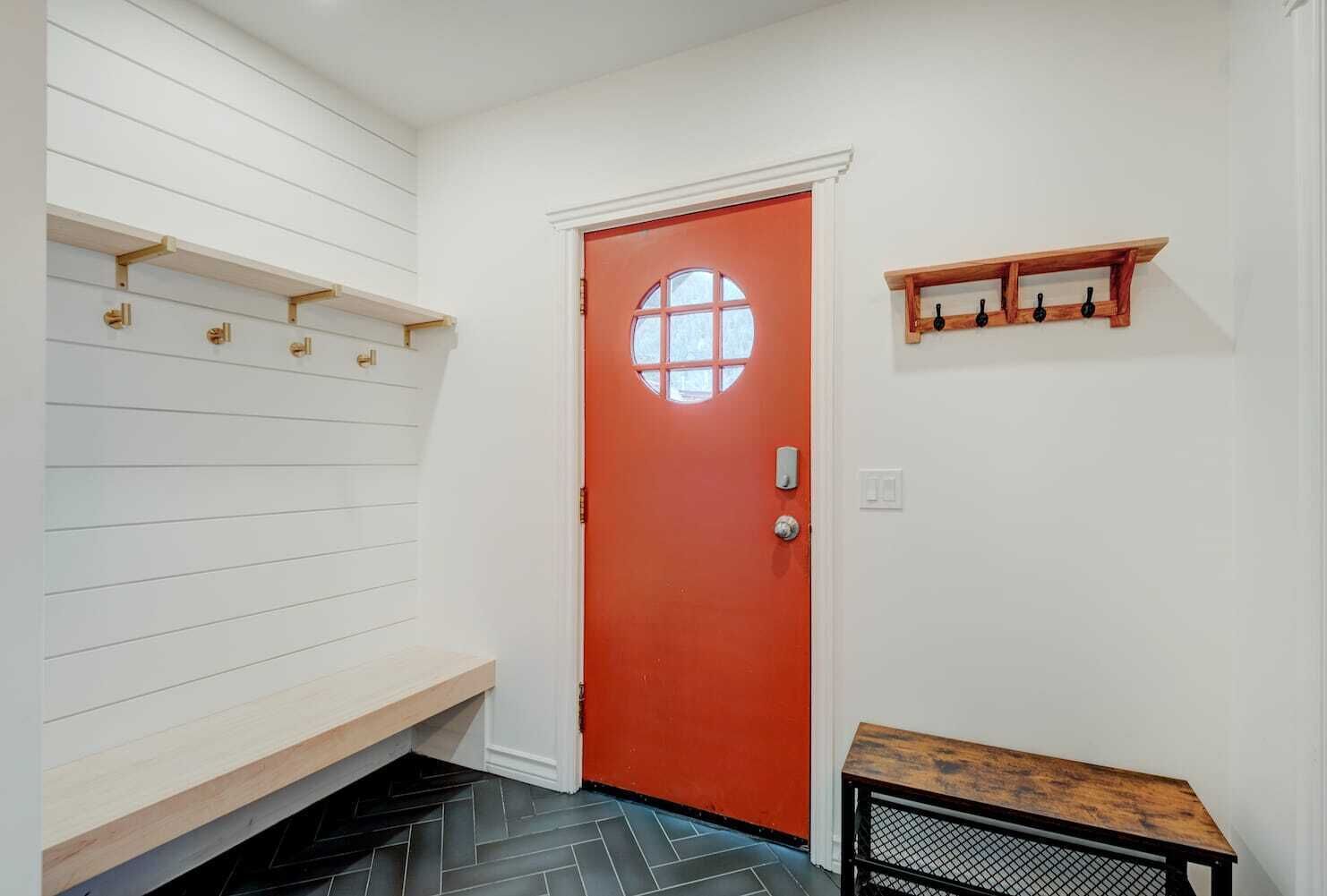 A hallway with a red door, white walls, and a bench.