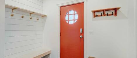 A hallway with a red door, white walls, and a bench.