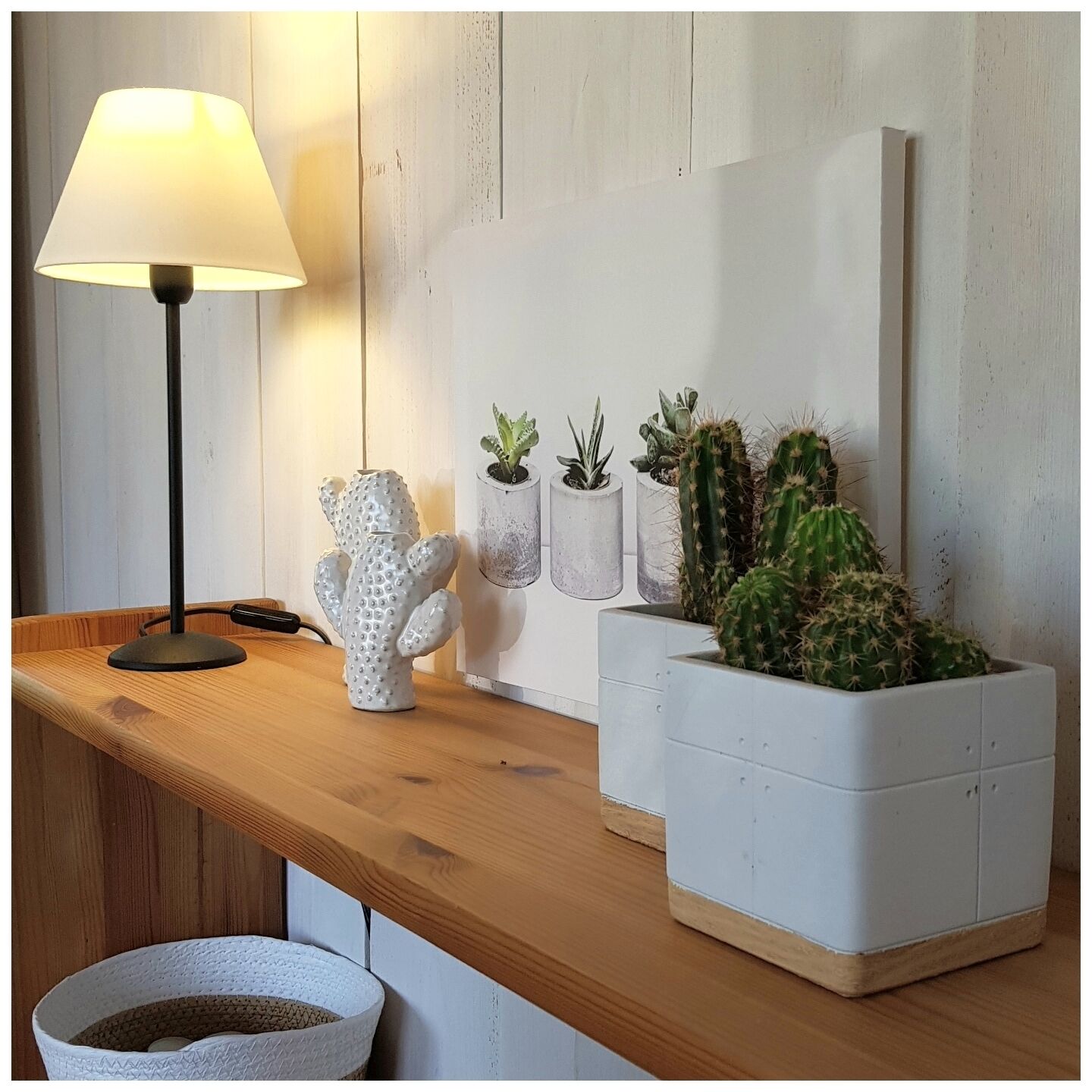 Une table en bois, une lampe, une sculpture de cactus et plusieurs plantes en pot.