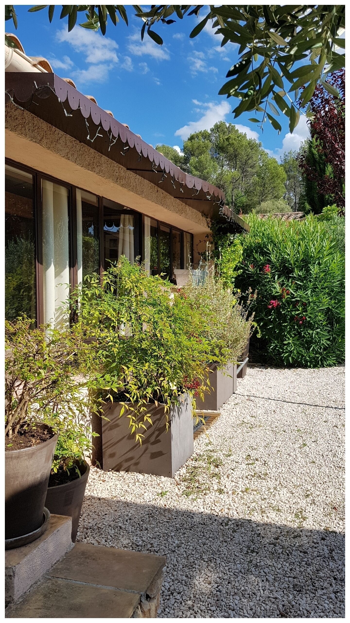 Un bâtiment doté d’un toit recouvert de tuiles, de grandes fenêtres et d’un chemin de gravier menant à une terrasse en bois.