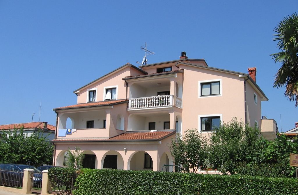 A two-story building with a balcony, arched windows, and a tiled roof.