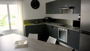 Une cuisine moderne avec des meubles gris, un four encastré et un réfrigérateur en acier inoxydable.