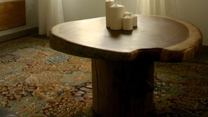 Une pièce avec une table ronde en bois, un tapis à motifs, une fenêtre avec des rideaux et une vue sur la verdure à l’extérieur.