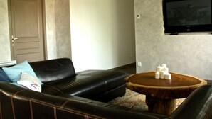 Un salon avec un canapé en cuir noir, une table basse en bois et un téléviseur à écran plat fixé au mur.