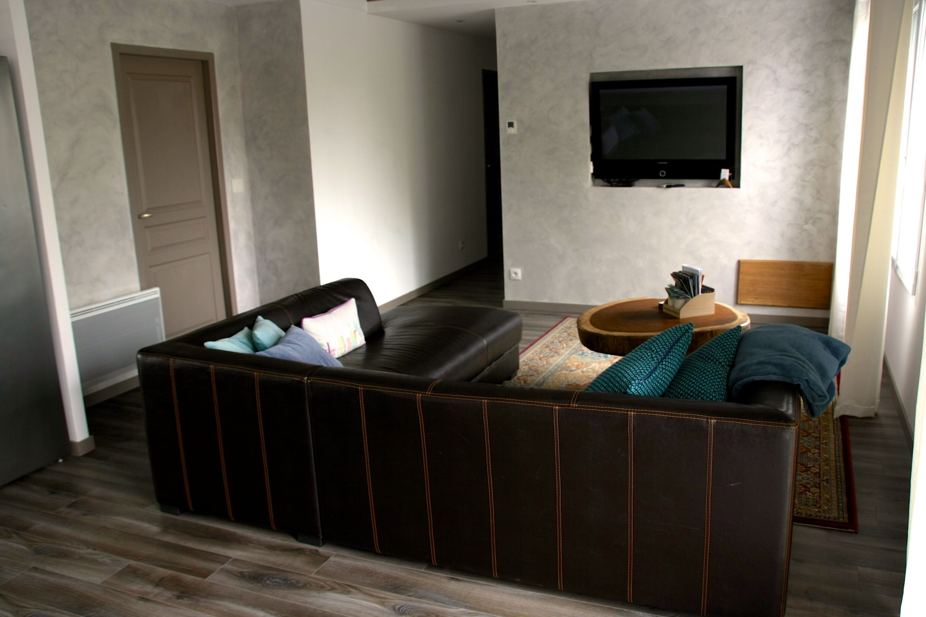 A modern living room with a sectional sofa, a flat-screen TV mounted on the wall, and a wooden coffee table.