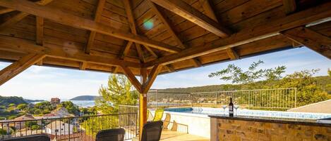 A wooden pergola with a pool and chairs overlooking a scenic landscape.