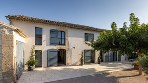 A two-story building with a tiled roof, large windows, and a paved courtyard with potted plants. - Farmhouse fully renovated in provence - Superb swimming pool 9m X 9m (Cavaillon)