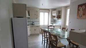 A compact kitchen with white cabinets, a glass dining table, and wooden chairs.