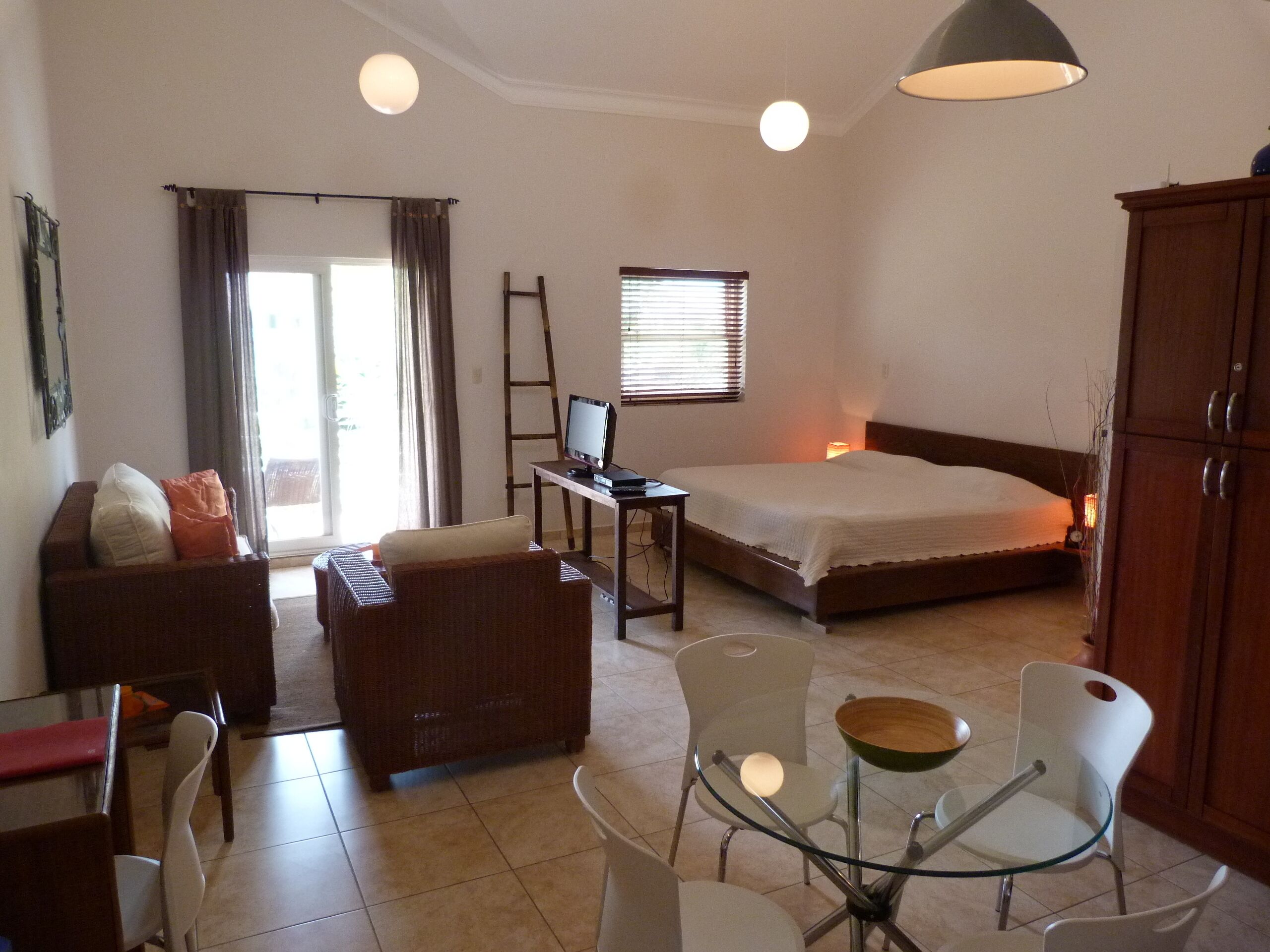 Un dormitorio con cama, escritorio con computadora, sofá y zona de comedor con sillas y mesa.