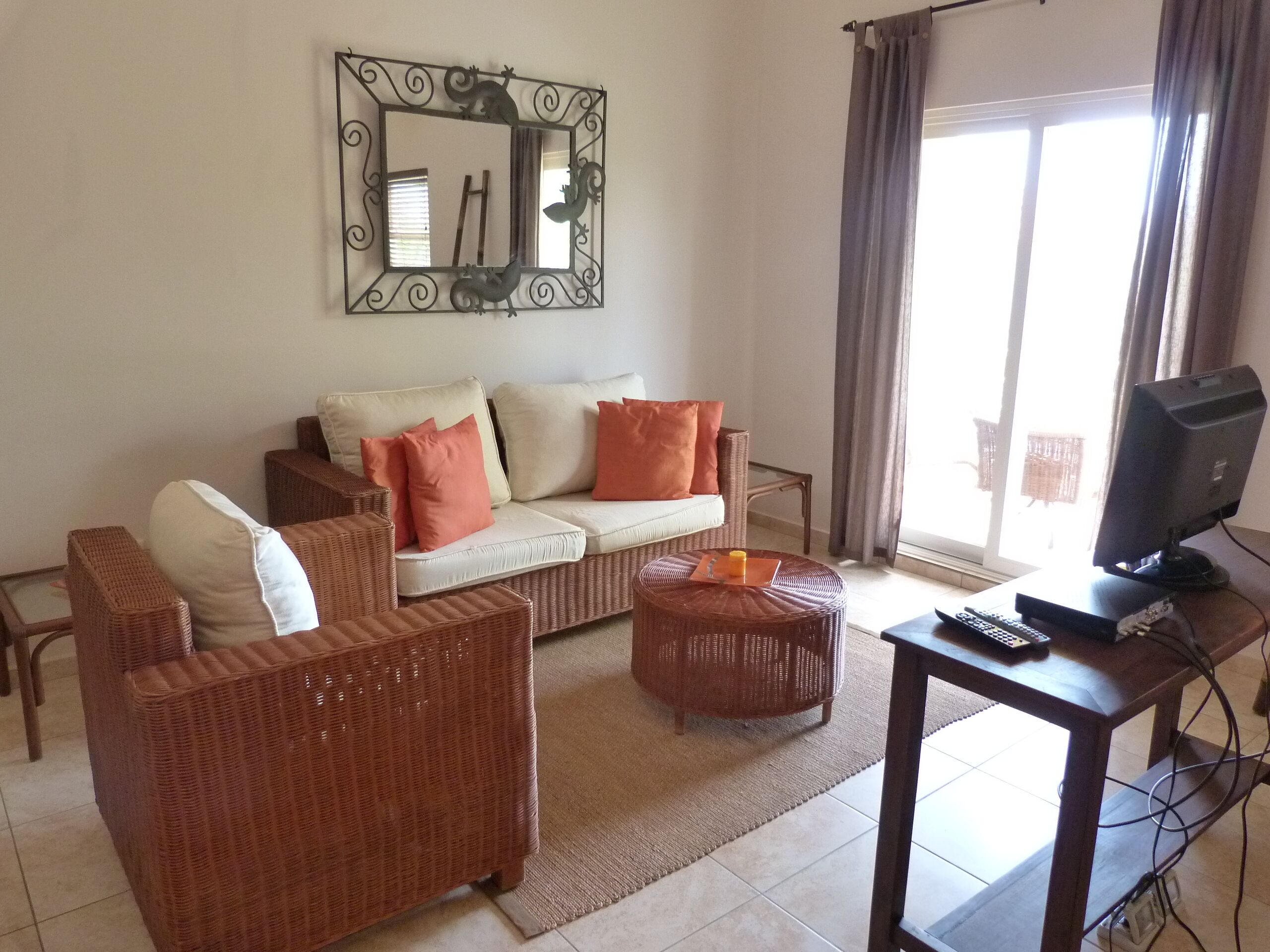 A living room with a sofa, two armchairs, a coffee table, a TV on a stand, and a large mirror on the wall.