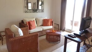 A living room with a sofa, two armchairs, a coffee table, a TV on a stand, and a large mirror on the wall. - Ocean Front studio for 2, Cabarete (Cabarete)