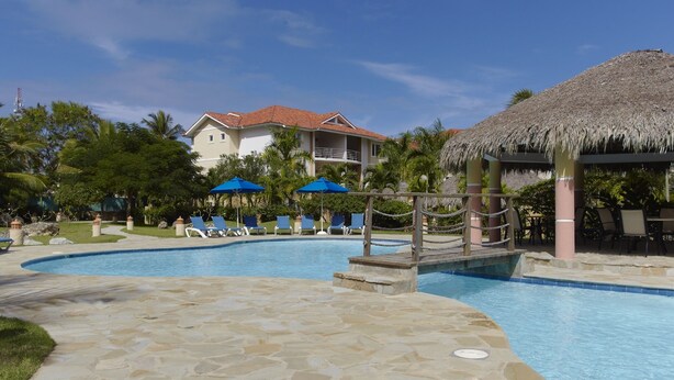 A pool area with lounge chairs, umbrellas, and a thatched-roof structure. - Ocean Front studio for 2, Cabarete (Cabarete)