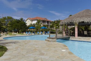 A pool area with lounge chairs, umbrellas, and a thatched-roof structure. - Ocean Front studio for 2, Cabarete (Cabarete)