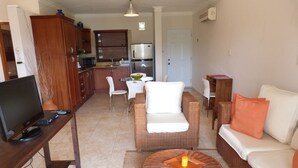 A living room with a TV, white chairs, a sofa, and a round wicker coffee table. - Ocean Front studio for 2, Cabarete (Cabarete)