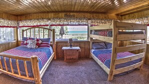 Una habitación tipo cabaña de madera con literas, una mesita de noche pequeña y una ventana con vistas.