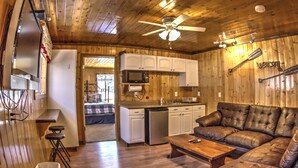 Un interior de cabaña acogedor, con paredes de madera, una zona de comedor, una cocina con armarios blancos y un sofá de cuero.