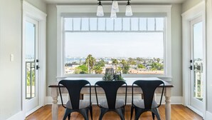 A dining area with a table and chairs, a large window with a city view, and a chandelier.