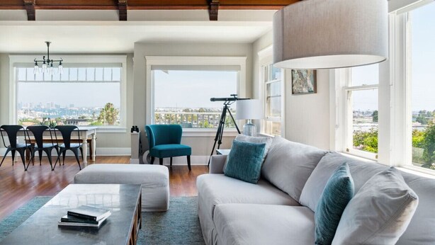A spacious living room with a large window, a sofa, a coffee table, and a tripod lamp.