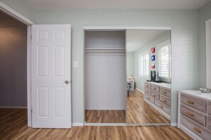 A room with a white door, a mirror, a dresser, and a window with blinds.