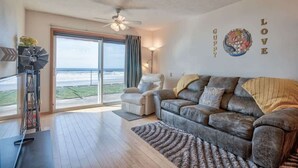 Un salón espacioso con un sofá de cuero, una silla y vistas al océano a través de grandes puertas correderas.