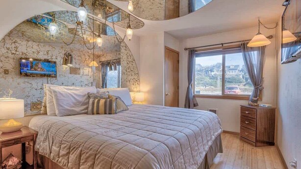 Un dormitorio con una cama, un televisor, un aparador de madera y una ventana con cortinas.
