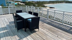 A wooden deck with a table and chairs, overlooking a beach and ocean. - Seaweed  Cottage   With Atlantic Ocean  View (exuma)