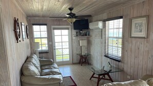 A room with a sofa, a glass table, a ceiling fan, and a TV. - Seaweed  Cottage   With Atlantic Ocean  View (exuma)