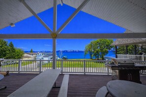 Un espace extérieur abrité, avec vue sur un lac et des montagnes, comprenant des tables de pique-nique et un barbecue.