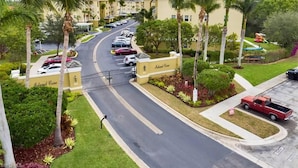 Un complexe hôtelier sécurisé, avec un accès contrôlé, une route sinueuse, des palmiers et un parking.
