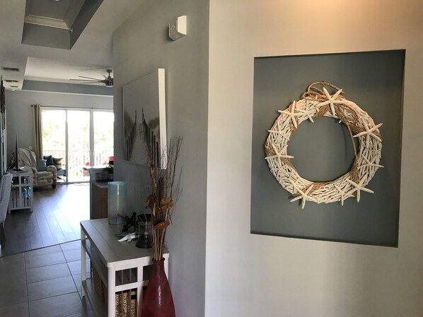 Una sala moderna con un ventanal grande, un adorno de estrella de mar en la pared y un jarrón con ramas secas sobre una consola blanca.