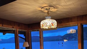 A cozy cabin interior with a large window overlooking a lake, a ceiling fan, and a cushioned seating area.