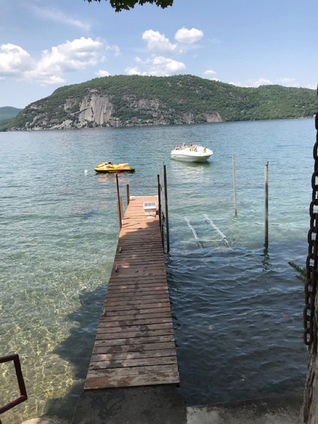 Une jetée en bois s’étendant dans un lac aux eaux claires, une colline rocheuse en arrière-plan et deux bateaux sur l’eau.
