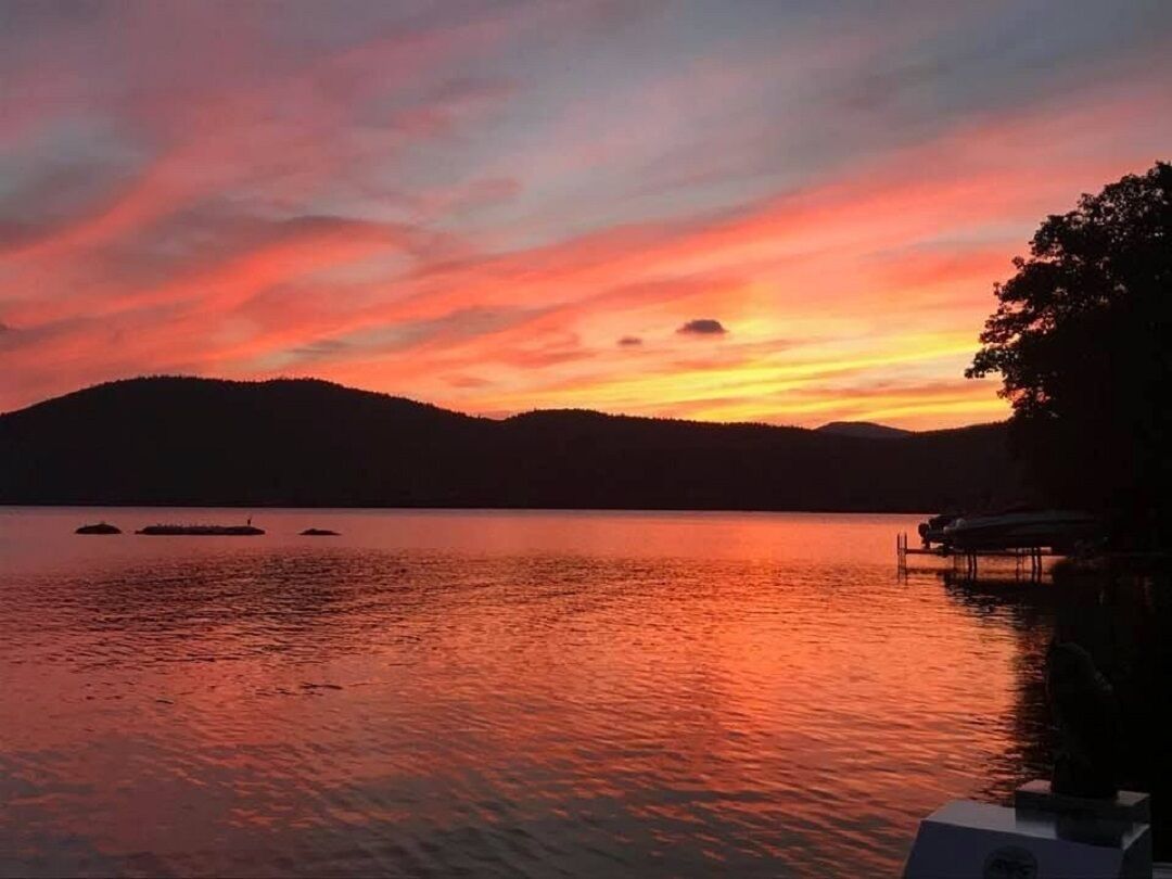 A sunset over a calm lake with boats and a dock.