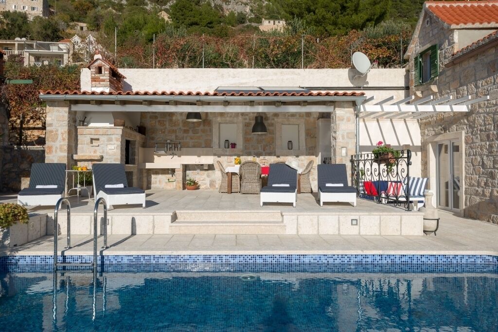A poolside area with lounge chairs, a stone building with a tiled roof, and a clear blue pool.