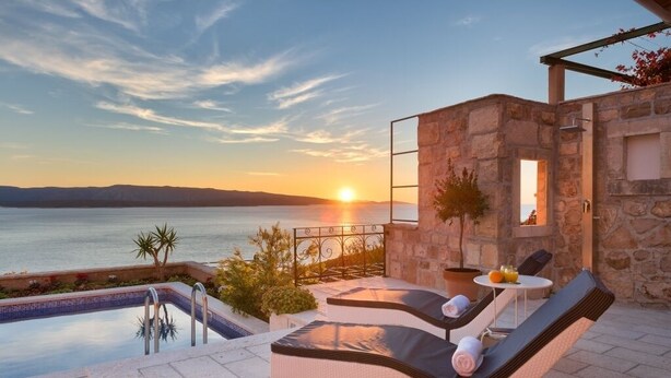 A poolside area with lounge chairs, a stone wall, and a view of the sea at sunset. - Holiday Home in Murvica with Seaview, Terrace, Air condition, WIFI (3756-1) (Murvica)