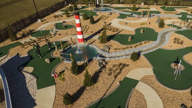 A miniature golf course with a lighthouse, winding paths, and small trees.