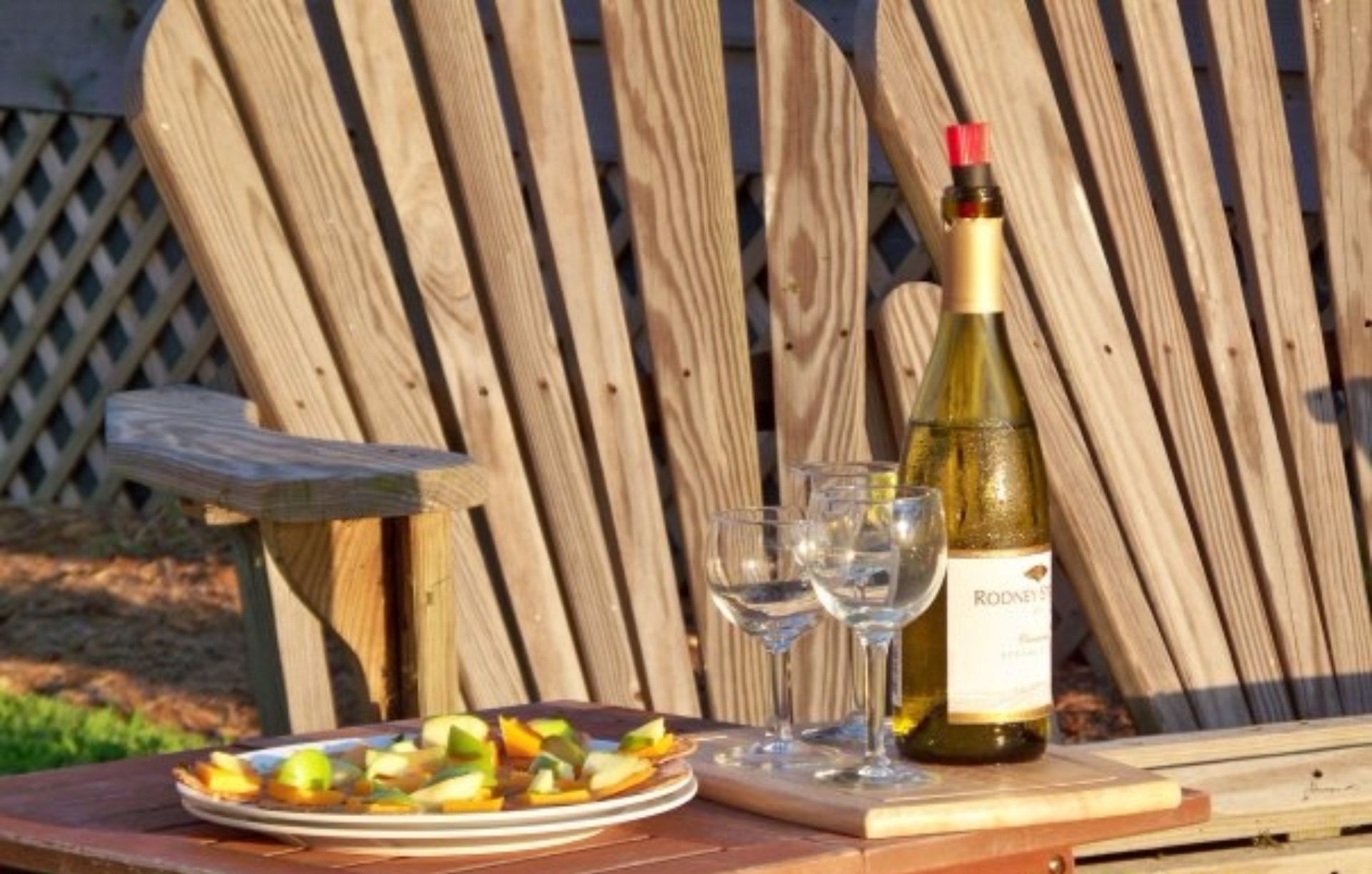 Een houten tafel met een fles wijn, twee glazen en een schaal fruit.