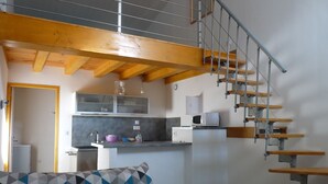 A compact living space with a kitchen, a staircase, and a sofa with a geometric-patterned cushion. - La Réserve, 2/4 person duplex gite, 9x4 pool, Saintes / Royan / Oléron axis (Luchat)