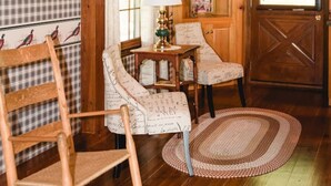 A cozy room with wooden flooring, a rocking chair, two upholstered chairs, a small table with a lamp, and a wooden door with a window.