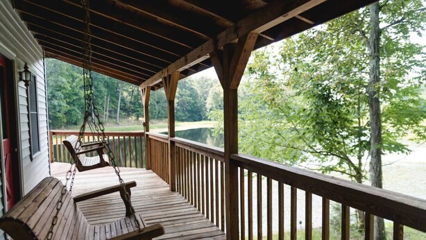 A wooden deck with a swing chair and a view of a lake.