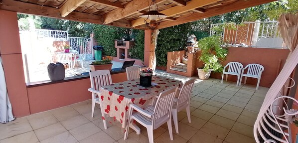 An outdoor patio with a table and chairs, surrounded by potted plants and a decorative fence.