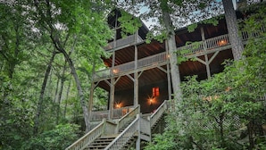 A multi-level wooden cabin with outdoor staircases surrounded by dense forest.