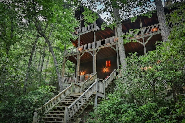 A multi-level wooden cabin with outdoor staircases surrounded by dense forest.