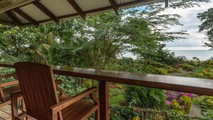 A wooden deck with a railing overlooking a lush garden and the ocean. - Ocean View #2 (Puerto Viejo)