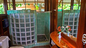 A bathroom with a toilet, a shower with a glass door, and a vanity with a mirror and a vase of flowers. - Ocean View #2 (Puerto Viejo)