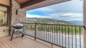 Un balcon avec un mur en pierre, un barbecue et une vue sur les montagnes et une route.