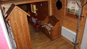 Una habitación de madera con una cama, un perchero y un ventanal con cortina.