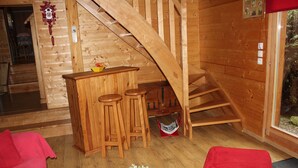 Interior de una cabaña de madera con escalera de madera, una pequeña zona de bar y un banco rojo.