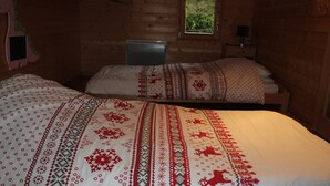 Una habitación acogedora de estilo cabaña con una cama grande con un edredón estampado, un escritorio pequeño con una lámpara y una ventana con vistas a la vegetación.